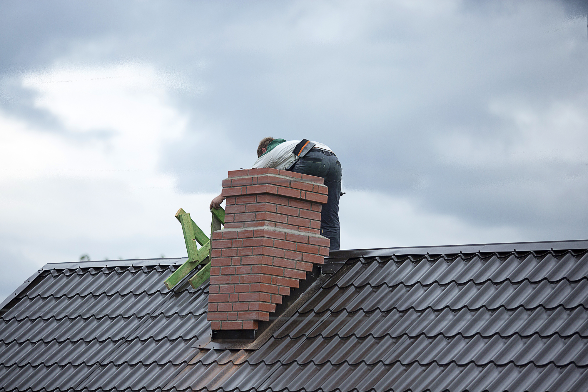 Worker repairing brick chimney on a roof